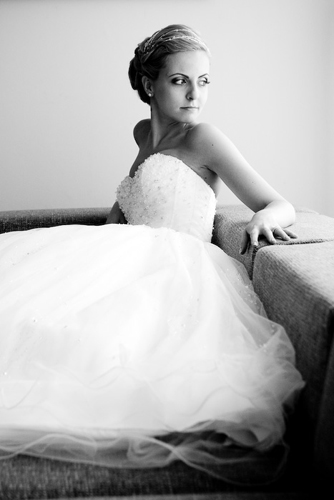 Braut sitzt im voluminösen Hochzeitskleid auf einem Sofa.